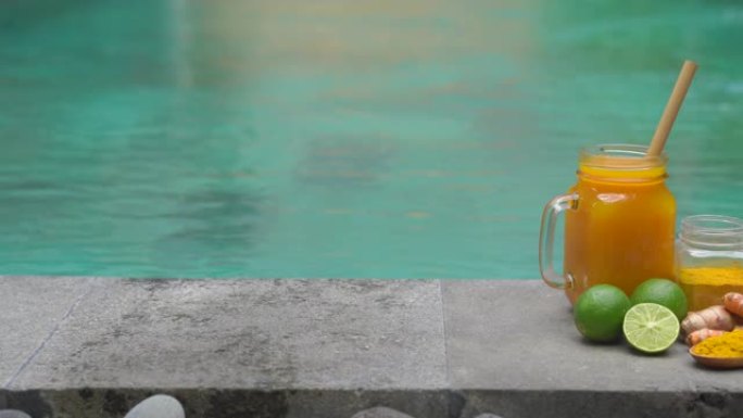 一杯带有民族巴厘岛饮料的玻璃杯，它是一种成分-站在游泳池边的姜黄，金鸡和酸橙