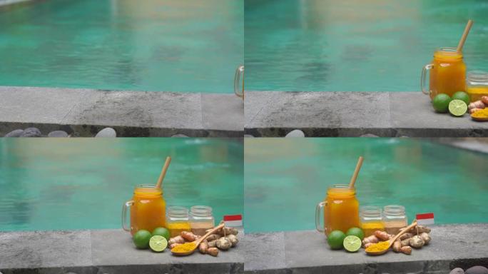 一杯带有民族巴厘岛饮料的玻璃杯，它是一种成分-站在游泳池边的姜黄，金鸡和酸橙
