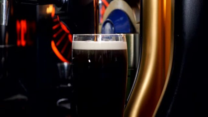 慢动作将工艺黑啤酒倒入玻璃中。新鲜和泡沫。酒吧背景。微型啤酒精酿啤酒。用高速相机拍摄，高清拍摄