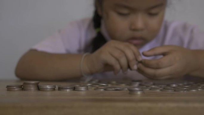 可爱的亚洲小女孩玩硬币赚成堆的钱，孩子为未来的概念存钱