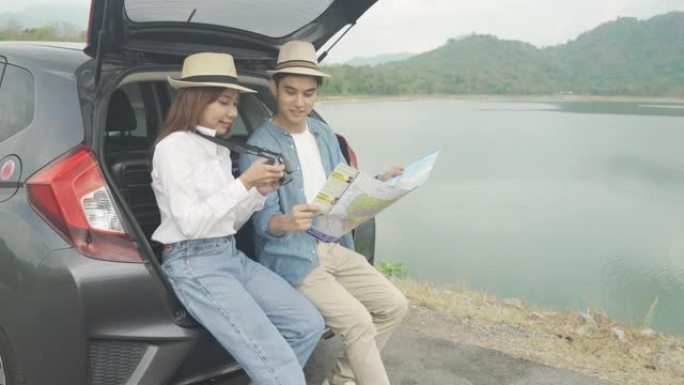 亚洲夫妇坐在车里的肖像，男人和女人在相机里看着照片，在度假时拿着地图。快乐的浪漫时光。