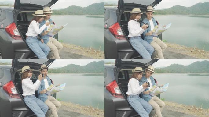 亚洲夫妇坐在车里的肖像，男人和女人在相机里看着照片，在度假时拿着地图。快乐的浪漫时光。