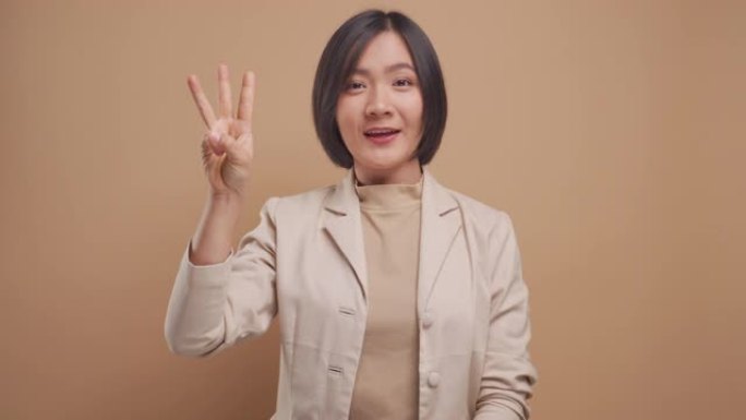 亚洲女商人显示用手指计数数字，微笑孤立在米色背景。4k视频