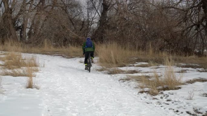 背着背包的男骑自行车者正在雪道上骑旅行自行车