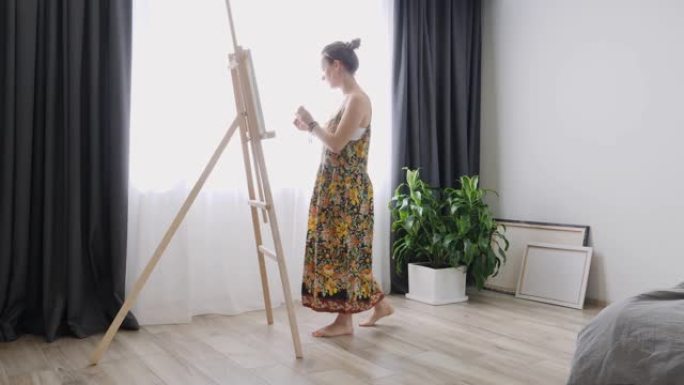 有才华的年轻女孩用手刷在画布上画画。家庭工作室的女艺术家站在画架附近，在画布上画画。绘图过程。灵感