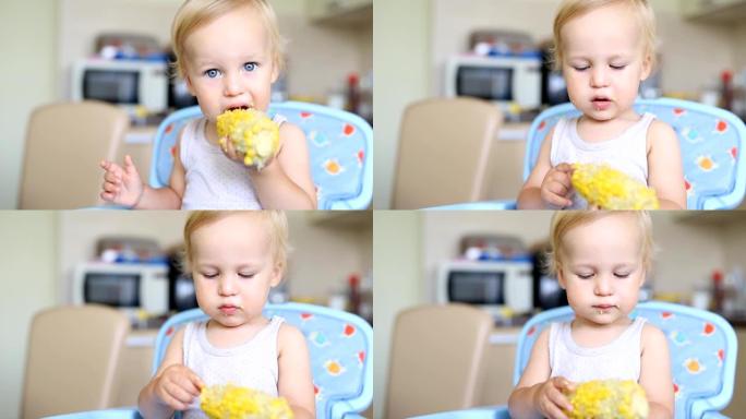 可爱的白人金发男孩坐在厨房的高脚椅上，喜欢吃美味的甜玉米。