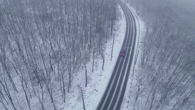 红色汽车在高速公路上行驶，在降雪下穿过森林的弯道上驶近。无人机航拍视频随着汽车的旋转和后退摄像机运动