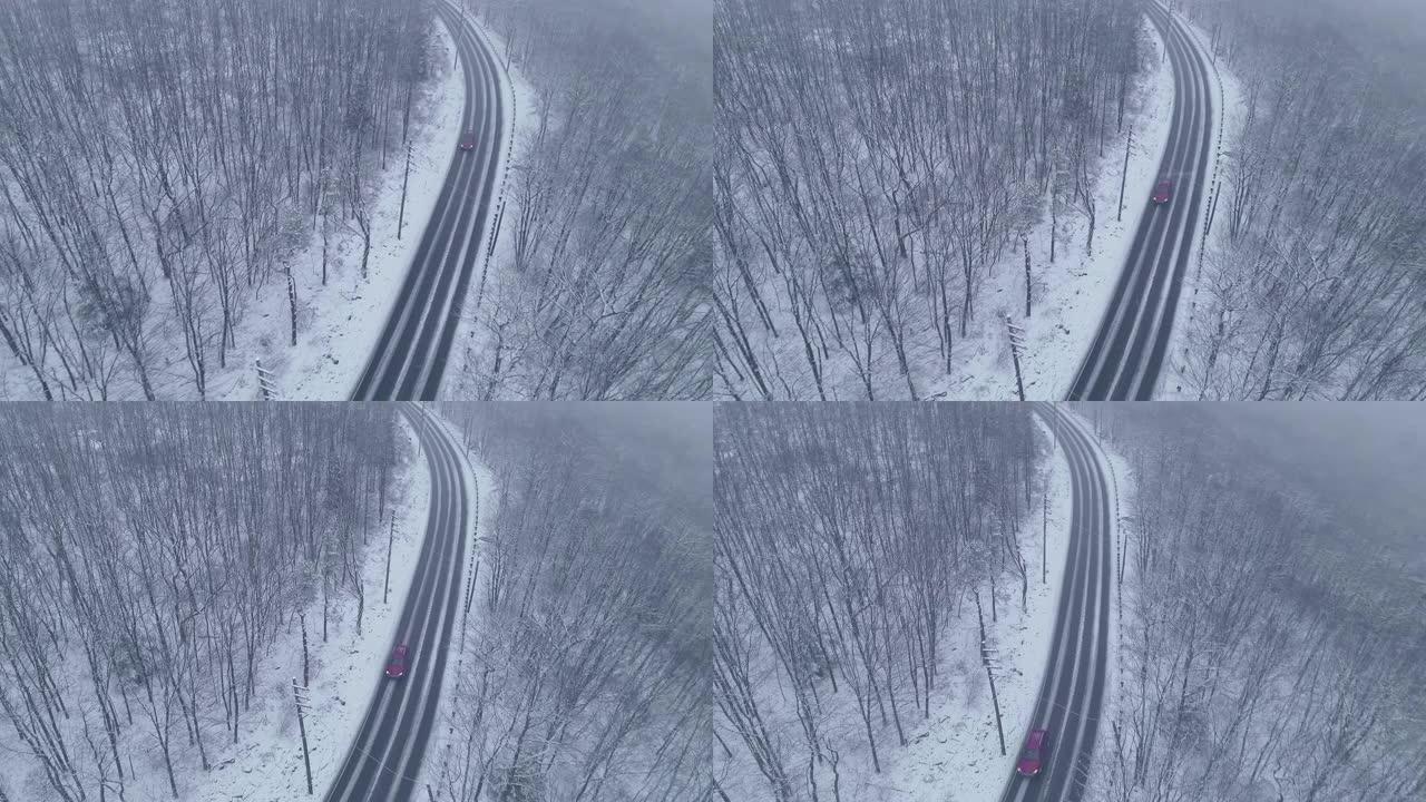 红色汽车在高速公路上行驶，在降雪下穿过森林的弯道上驶近。无人机航拍视频随着汽车的旋转和后退摄像机运动
