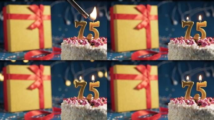 白色生日蛋糕75号点火器燃烧的金色蜡烛，蓝色背景带灯和用红丝带绑起来的礼物黄色盒子。特写