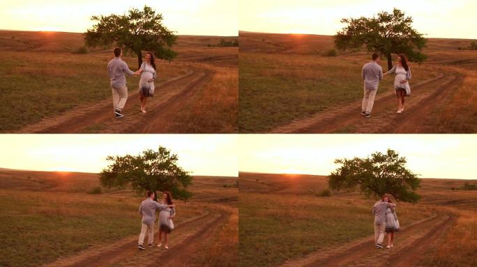 幸福的孕妇和她的丈夫在日落时沿着乡间小路行走