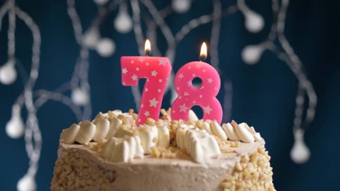 蓝色背景上有78号粉色蜡烛的生日蛋糕。蜡烛吹灭了。慢动作和特写视图