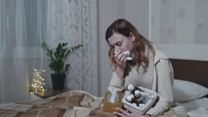 生病的女孩因感冒或流感咳嗽而感到喉咙痛，用餐巾纸捂住嘴，坐在沙发上时将药物浸入温暖的毯子中