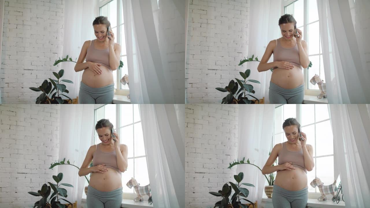孕妇在家打电话。准妈妈抚摸着裸露的腹部