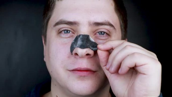 一名男子穿上并从黑点上取下一条鼻子。黑头和粉刺的煤炭清洁条。个人护理的概念。