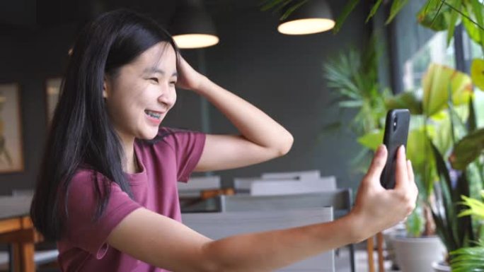 年轻快乐的亚洲千禧一代女子自拍，在咖啡馆里用牙套微笑，积极的女少年