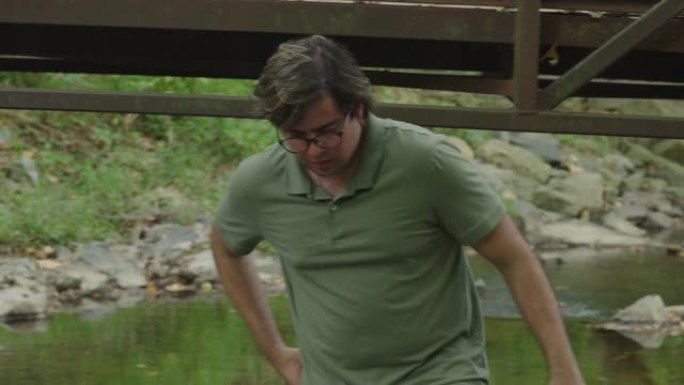 一名男子从桥上跑到一条小溪上，从水中拔出手机。