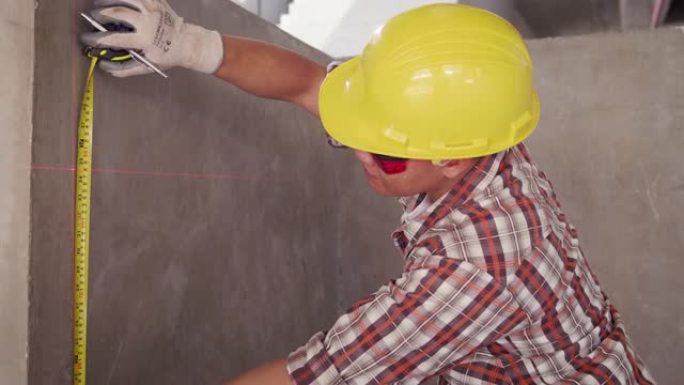 施工现场用胶带测量安全帽测量墙的亚洲建筑工程师，现场测量工作期间用激光水平仪检查建筑项目的工作工程师