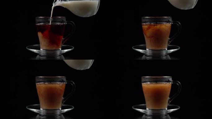 在玻璃茶杯和茶托中的红茶中，从黑色背景上的玻璃壶中倒牛奶，慢动作拍摄