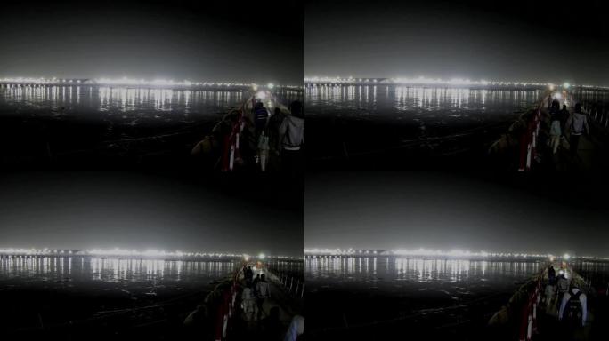 当地人在跨sangam的桥上走到另一侧的Kumbha Mela营地灯