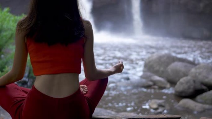 后视亚洲女性在瀑布练习或做瑜伽，莲花在冥想会上摆姿势。美丽的风景，自然的背景，泰国。