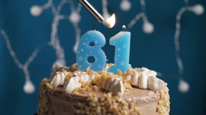 蓝色背景上有61号蜡烛的生日蛋糕。蜡烛着火了。慢动作和特写视图