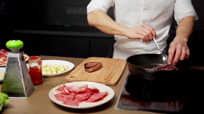 面目全非的厨师在平底锅上煎牛肉牛排，并用叉子将现成的肉放在木制切菜板上