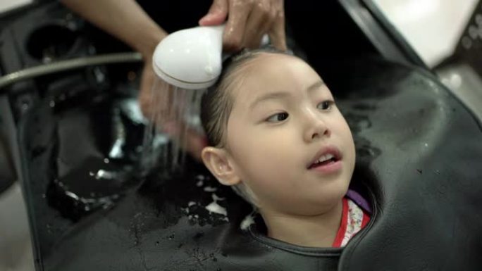 亚洲小女孩在美容院洗头。理发师给她的客户洗头。小女孩有幸福，喜欢洗头。手持镜头，真实生活