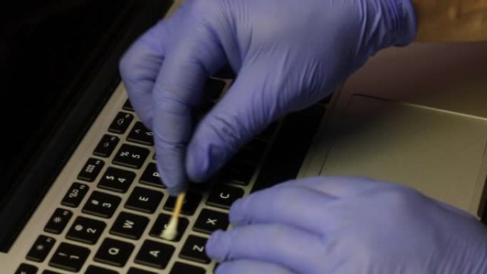 一个戴着橡胶手套的男人正在清洁他的笔记本电脑。棉签清洁钥匙。然后他用特殊的餐巾擦拭笔记本电脑键盘。保