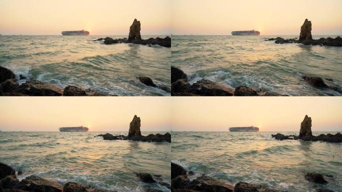 日落时与货船一起淹没在海中的大型岩石。海浪溅到淹没的岩石上。
