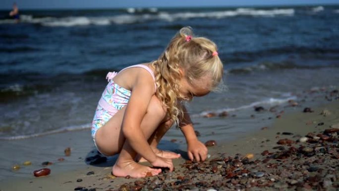 美丽的金发女孩在海上海岸线上玩鹅卵石。海浪