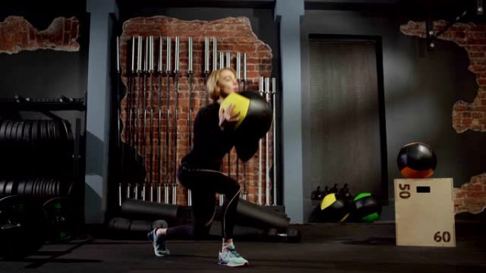 穿着黑色运动服的健康年轻女子在健身房交叉训练中拿着壁球做弓步