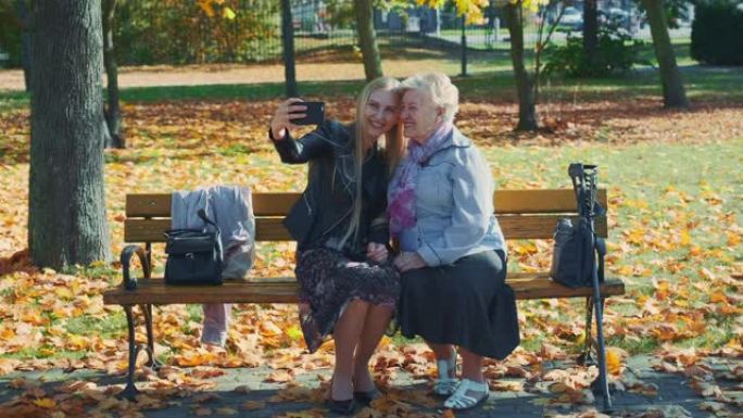 秋天在美丽的公园里，年轻人和老年妇女在智能手机上自拍的变焦镜头