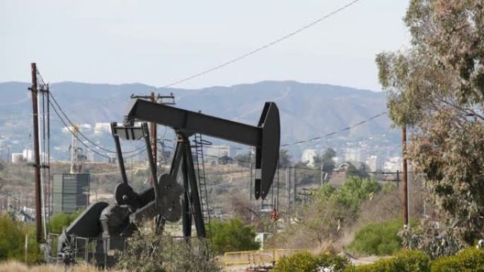 工业城市景观。洛杉矶的拉布雷亚·英格尔伍德。井泵千斤顶在栅栏后面运行。钻机开采原油。带工作活塞的采油