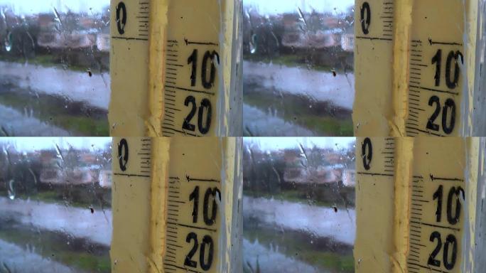 外面有雨的天气。窗户玻璃上的水滴，雾蒙蒙的温度计刻度