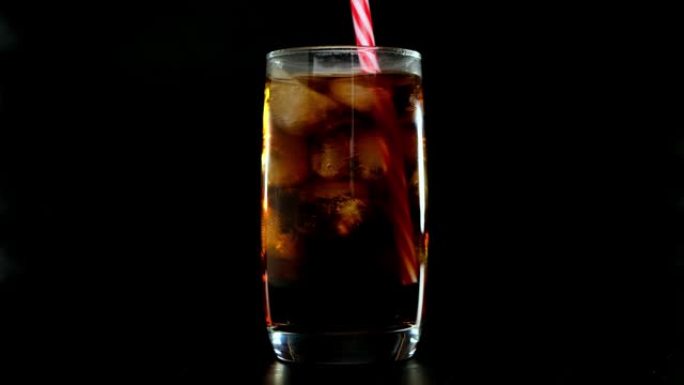 将稻草放入可乐中，玻璃冰块放在黑色背景上。