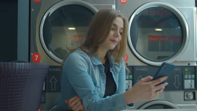 女人在自助洗衣店洗衣服时使用智能手机。