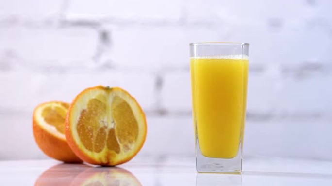 鲜榨橙汁放在桌子上的玻璃杯中，旁边有橙片。白色背景上有水果的清爽黄色饮料