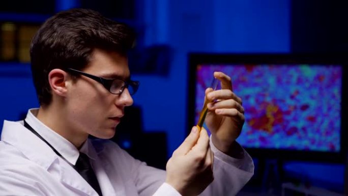 实验室外套和眼镜中专注的年轻男性科学家的侧视图仔细检查生化实验室中的黄色液体试管