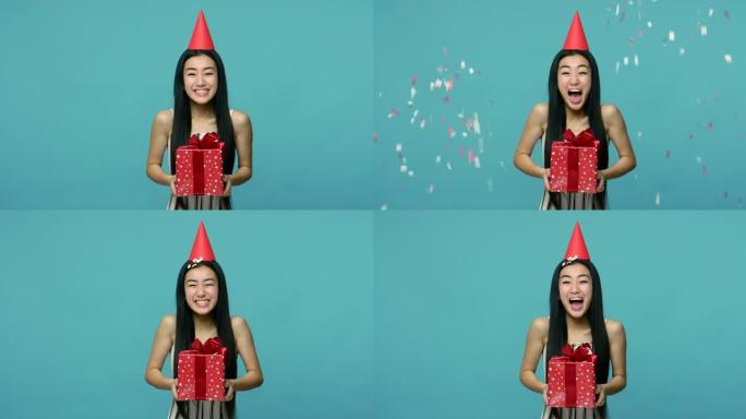 五彩纸屑落在兴奋的亚洲女人身上，头上有滑稽的派对锥，女孩拿着礼物盒子，接受问候