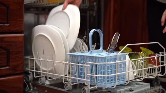 家庭主妇在午餐、晚餐或派对庆祝活动后给现代洗碗机装上脏餐具。两个洗衣机的篮子里装满了脏盘子，女人关闭