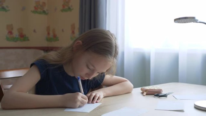 十几岁的女孩在窗户背景的桌子上用笔在纸上写字。女学生用钢笔在家庭办公室的桌子上的方格纸上写字。