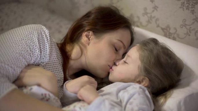 母亲和年幼的女儿躺在床上睡觉后互相拥抱，父母和孩子之间的关系。