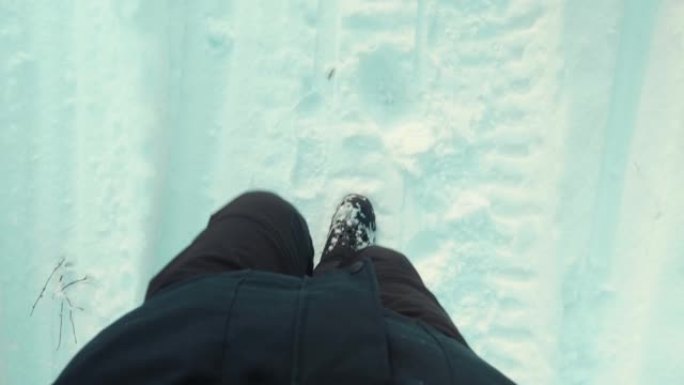 在白雪皑皑的小径上行走的无法辨认的男性脚的俯视图。穿靴子的家伙要踩在白色的雪上。面目全非的徒步旅行者