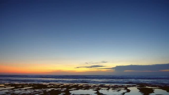 日落后黑暗海滩的全景，深蓝色的水