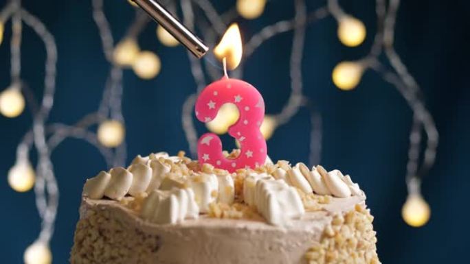 蓝色背景上有3个数字粉色蜡烛的生日蛋糕。蜡烛着火了。慢动作和特写视图
