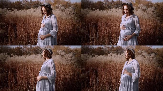 漂亮的孕妇在田野里用高蓬松的野草抚摸她的肚子