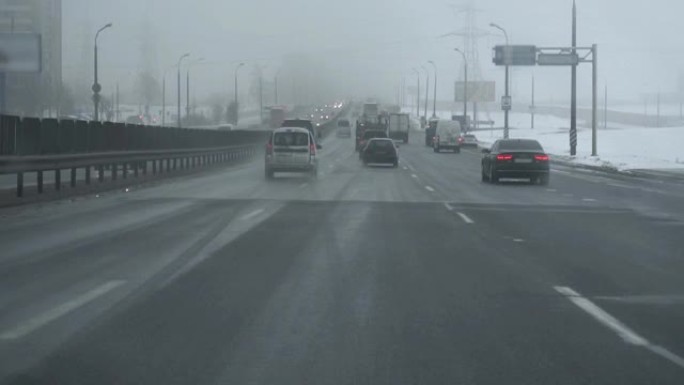 降雪时汽车在高速公路上行驶。从驾驶室内部通过挡风玻璃观看。冬天的白天。交通恶劣的天气条件，暴风雪。旅