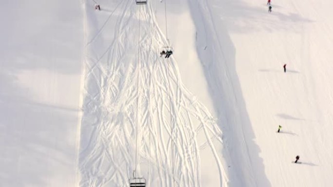 无人机飞越山区度假胜地雪坡上移动的滑雪电梯。顶部鸟瞰式滑雪缆车运送雪山上的滑雪者和滑雪者。雪域高原的