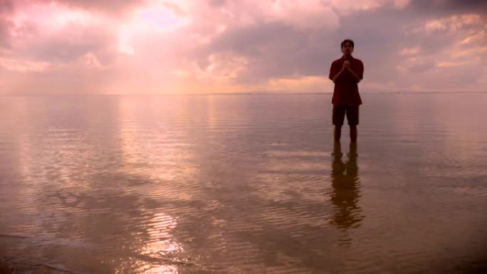 人站在平静的海洋水中，在日出时祈祷