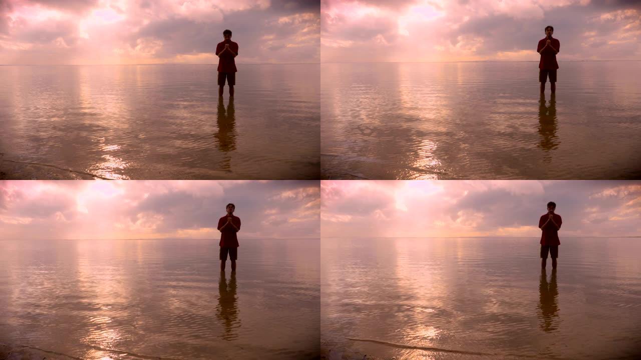 人站在平静的海洋水中，在日出时祈祷